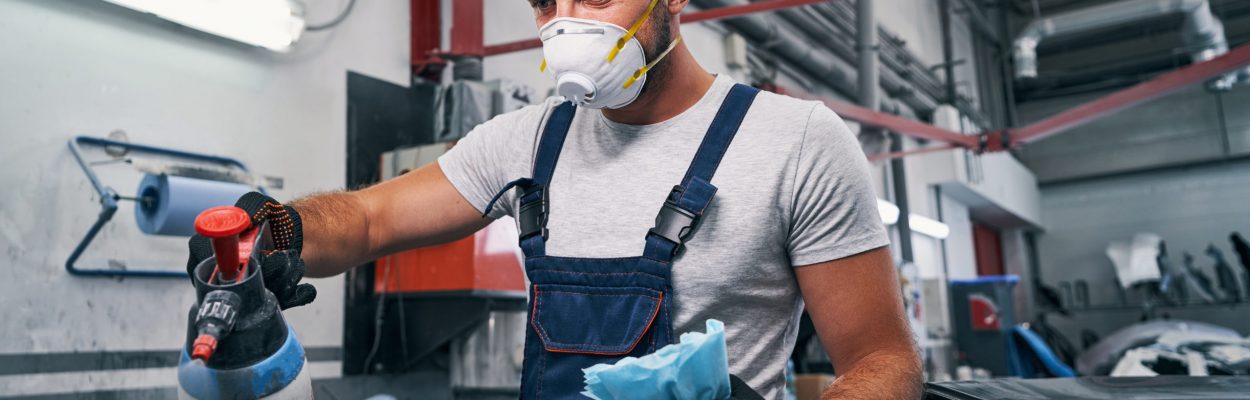 Automobile mechanic in workshop spraying car with cleaning fluid from bottle while holding paper towel